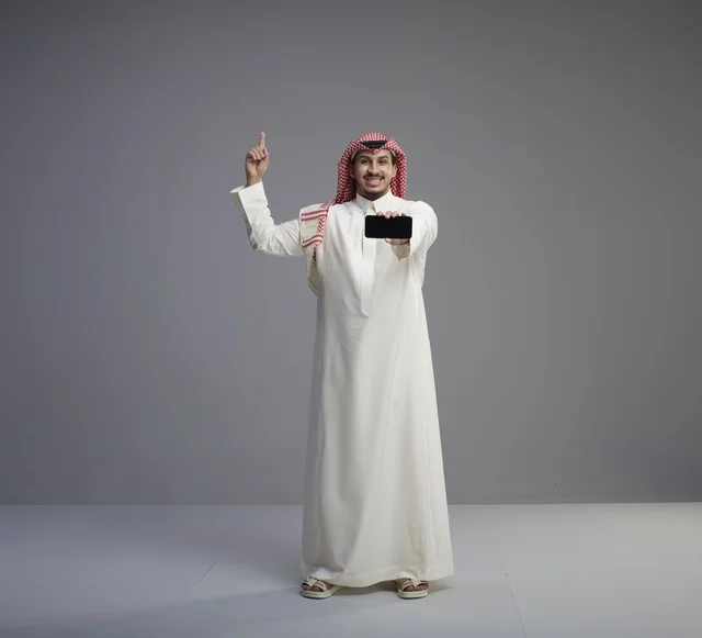 Saudi Man Holding Smartphone Pointing Up in Studio