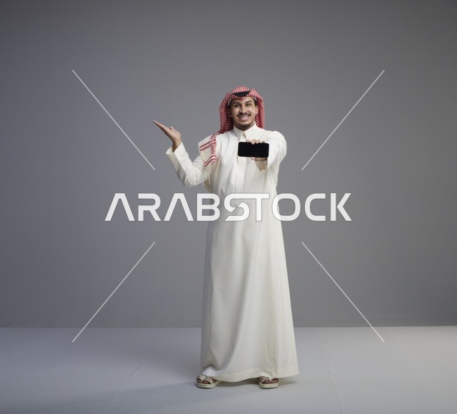 رجل سعودي يحمل نموذج هاتف ذكي خلفية رمادية