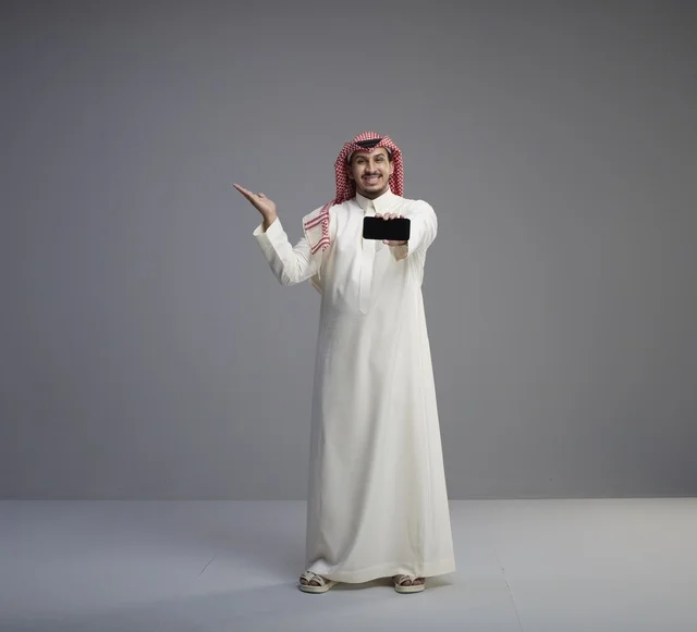 رجل سعودي يحمل نموذج هاتف ذكي خلفية رمادية
