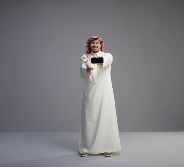 رجل سعودي يحمل نموذج هاتف ذكي في الاستوديو