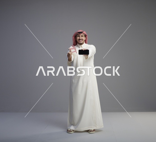 رجل سعودي يحمل هاتف ذكي مع إيماءة الإبهام