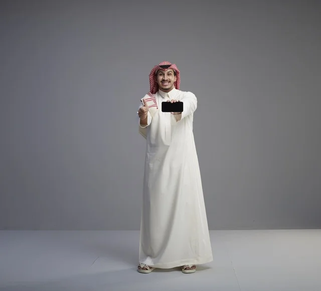 رجل سعودي يحمل هاتف ذكي مع إيماءة الإبهام