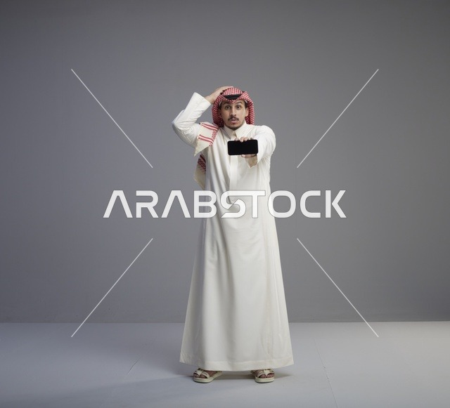 رجل سعودي يحمل هاتف ذكي بتعبيرات وجه مندهشة