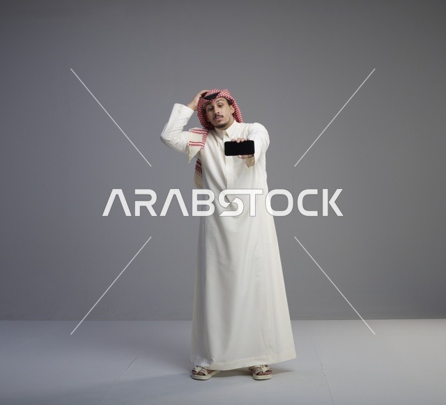 رجل سعودي يحمل هاتف ذكي بتعبير وجه محتار
