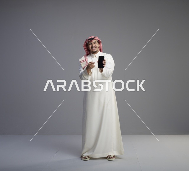 رجل سعودي يحمل نموذج هاتف ذكي بخلفية رمادية