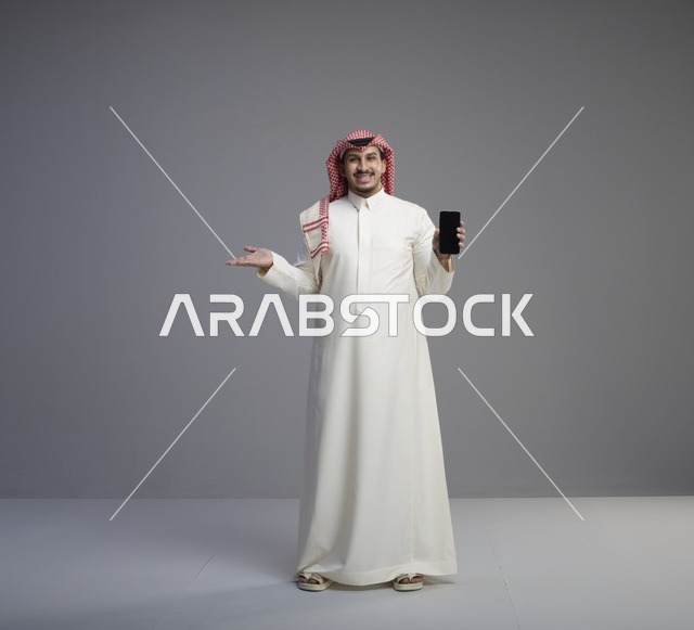رجل سعودي يحمل هاتف ذكي على خلفية استوديو رمادية