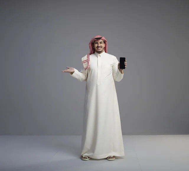 رجل سعودي يحمل هاتف ذكي على خلفية استوديو رمادية