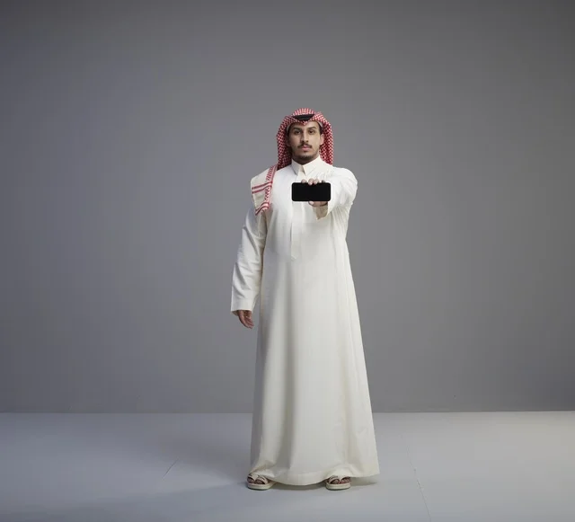 رجل سعودي يرتدي الثوب التقليدي يحمل نموذج هاتف ذكي