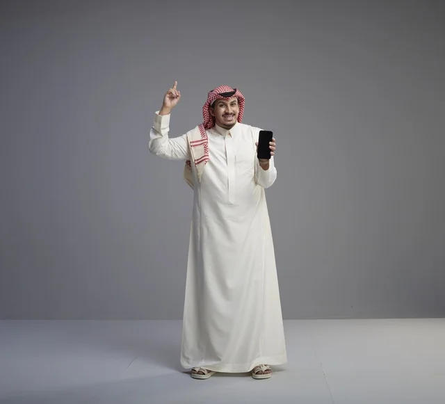 Saudi Man Holding Smartphone and Pointing Up in Studio