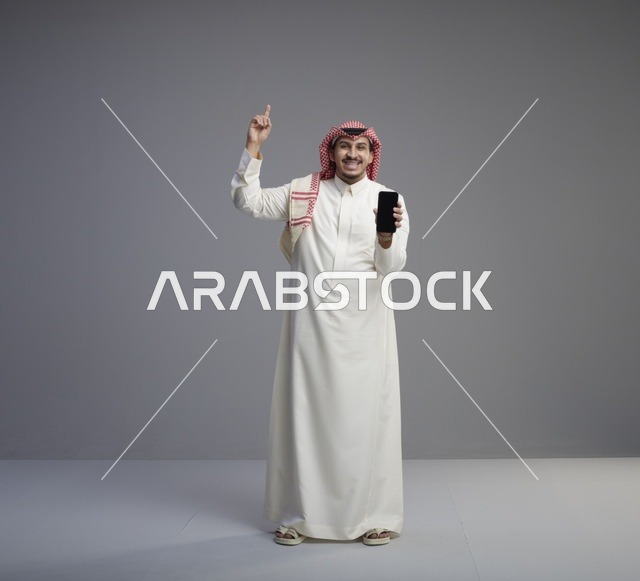 رجل سعودي يحمل هاتف ذكي ويشير للأعلى