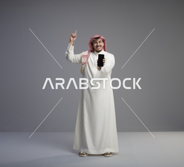 رجل سعودي يحمل هاتف ذكي ويشير للأعلى