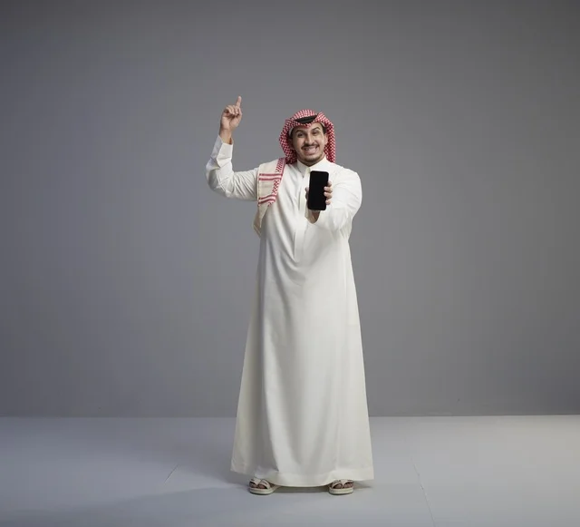 رجل سعودي يحمل هاتف ذكي ويشير للأعلى