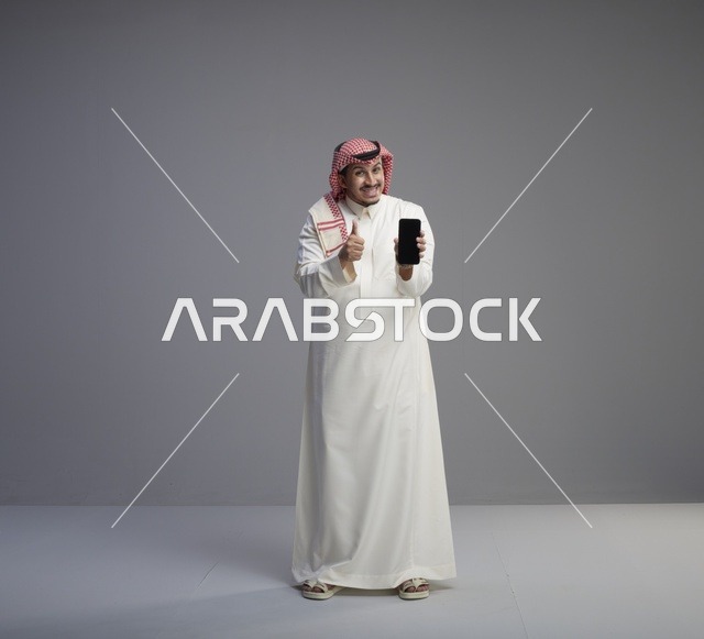 رجل سعودي يحمل هاتف ذكي مع إيماءة الإبهام للأعلى