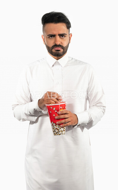 بورتريه لرجل عربي خليجي سعودي يحمل بيده علبة الفشار  ، مشاهدة الافلام والمسلسلات ، ايماءات وتعابير الوجه تدل على الملل ، افلام وسينما