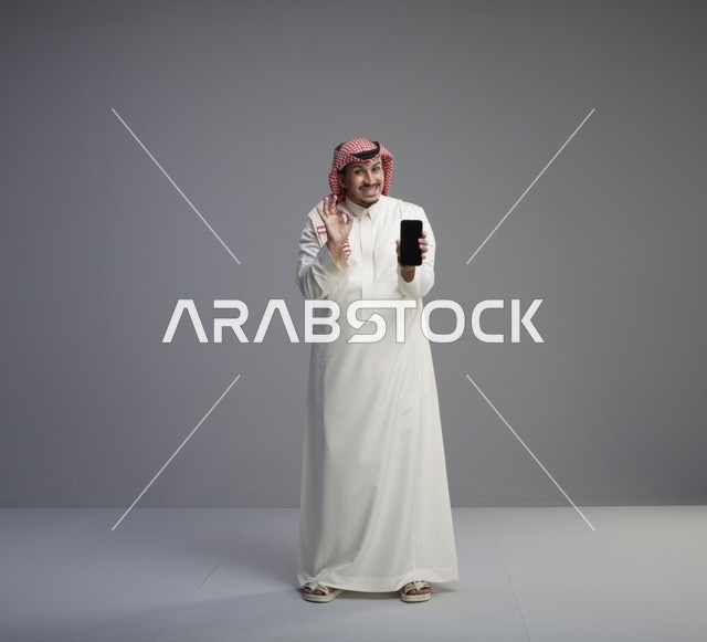 رجل سعودي يحمل هاتف ذكي بإشارة التمام في استوديو