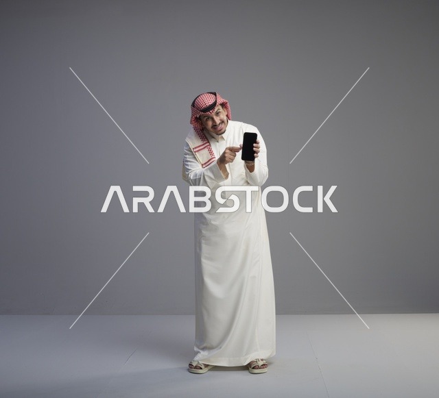رجل سعودي في استوديو يحمل هاتفاً ذكياً ويشير إليه