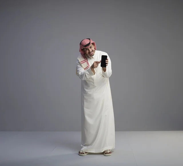 رجل سعودي في استوديو يحمل هاتفاً ذكياً ويشير إليه