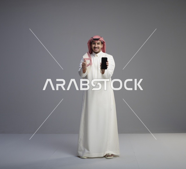رجل سعودي يحمل هاتف ذكي مع إشارة الإعجاب في الاستوديو