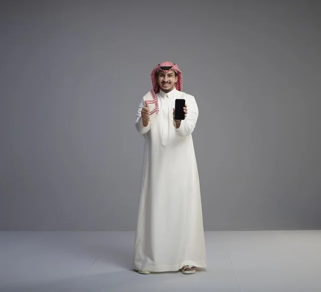 Saudi Man Holding Smartphone with Thumbs Up in Studio