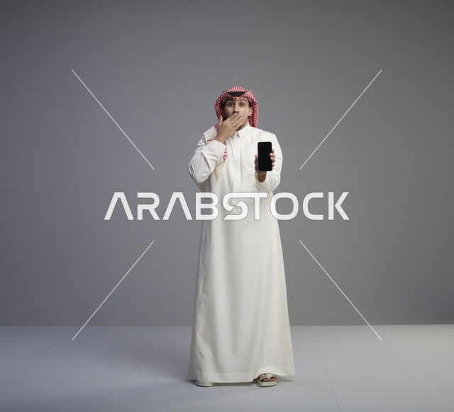 رجل سعودي مندهش يحمل هاتف ذكي في الاستوديو