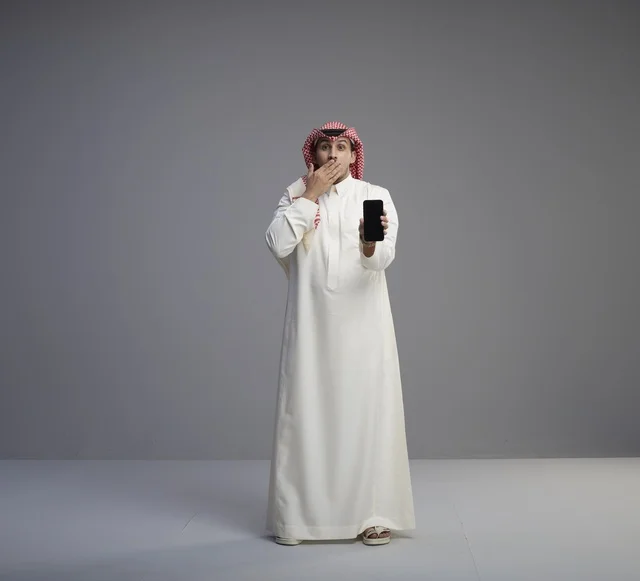 رجل سعودي مندهش يحمل هاتف ذكي في الاستوديو