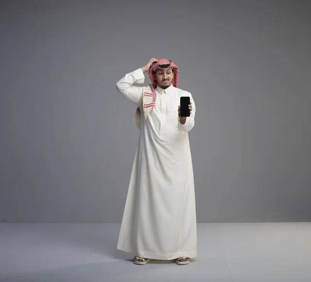Confused Saudi Man Holding Smartphone on Grey Background