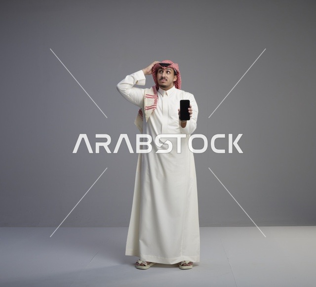 رجل سعودي يحمل هاتف ذكي بتعبير وجه محتار