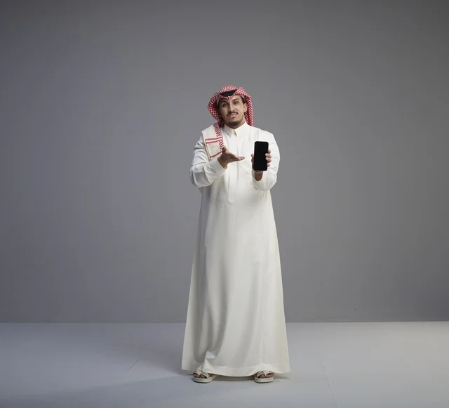 Saudi Man Holding Smartphone in Studio Grey Background