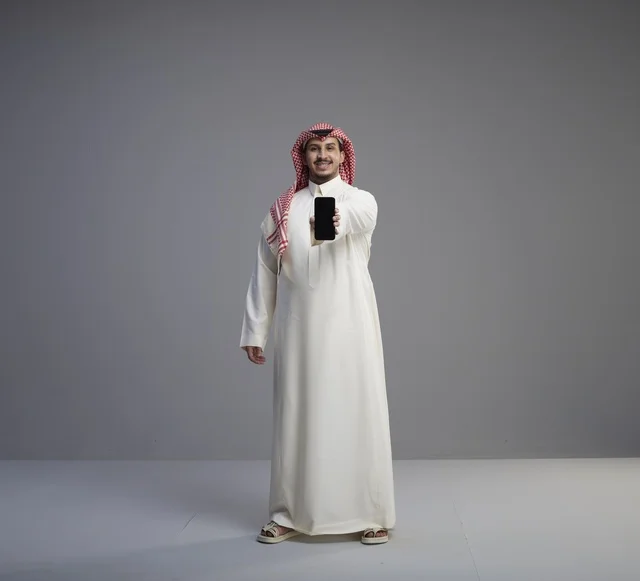 Saudi Man Holding Smartphone in Studio Grey Background