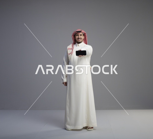 رجل سعودي يحمل نموذج هاتف ذكي في الاستوديو