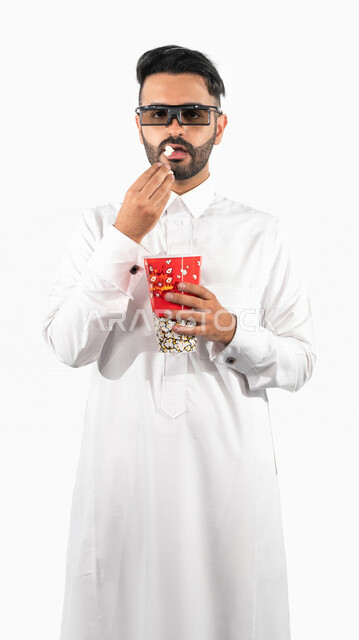 بورتريه لرجل عربي خليجي سعودي يرتدي نظارة ثلاثية الابعاد و يحمل بيده علبة الفشار ، ايماءات الوجه واليدين تدل على الحماس والدهشة ، مشاهدة الافلام داخل السينما ، متابعة افلام الاثارة والاكشن ، أفلام وسينما
