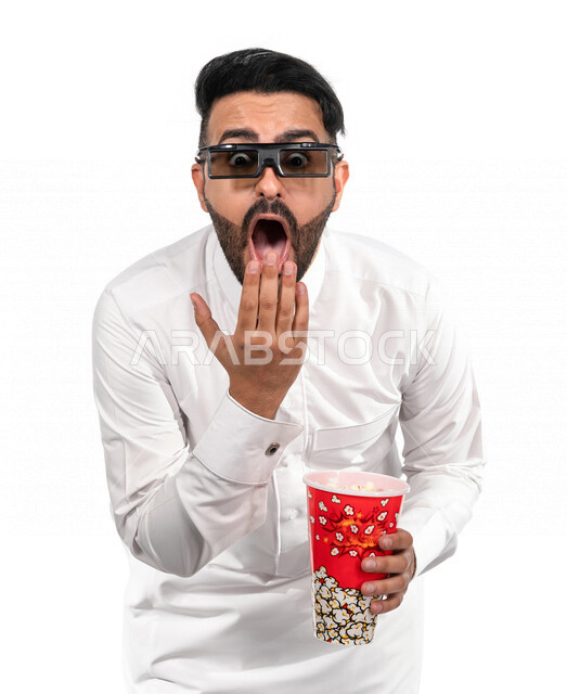 بورتريه لرجل عربي خليجي سعودي يرتدي نظارة ثلاثية الابعاد و يحمل بيده علبة الفشار ، ايماءات الوجه واليدين تدل على الحماس والدهشة ، مشاهدة الافلام داخل السينما ، متابعة افلام الاثارة والاكشن ، أفلام وسينما