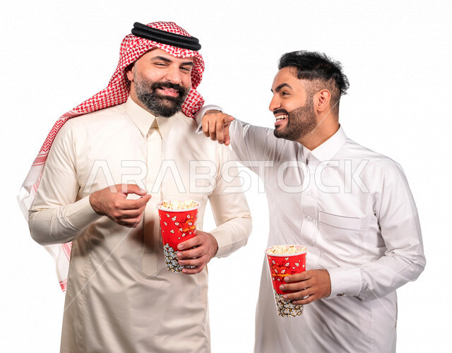 بورتريه لرجلان عربيان خليجيان سعوديان يحملان علبة الفشار ، ايماءات الوجه واليدين تدل على المرح والاستمتاع ، مشاهدة الافلام داخل السينما ، متابعة افلام ومسلسلات كوميدية  ، أفلام وسينما 