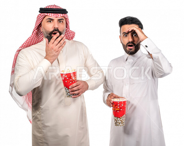 بورتريه لرجلان عربيان خليجيان سعوديان يحملان علبة الفشار ، ايماءات الوجه واليدين تدل على الحماس والدهشة ، مشاهدة الافلام داخل السينما ، متابعة افلام الرعب والاكشن ، أفلام وسينما 