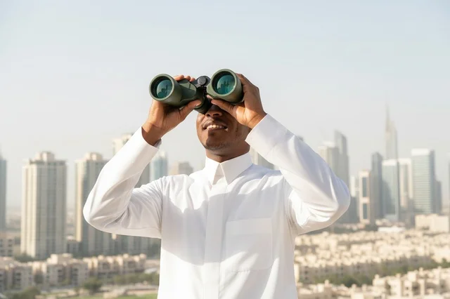 Emirati Man Using Binoculars with City Skyline Background