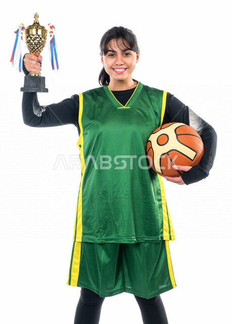 Portrait of a Saudi girl, wearing sports clothes, holding a basketball and a winning cup in her hand, with gestures indicating happiness with victory and victory, playing basketball, leisure and entertainment, game sports, women's sports activities in Sau