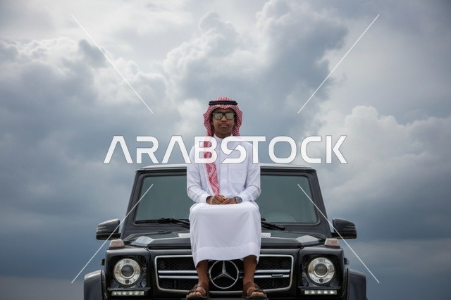 رجل سعودي مع سيارة دفع رباعي فاخرة تحت سماء غائمة