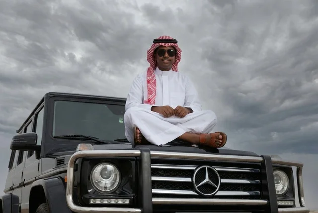 رجل سعودي بالثوب التقليدي يجلس على سيارة فاخرة