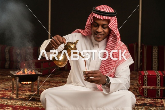 رجل سعودي بالزي التقليدي يصب القهوة العربية في خيمة