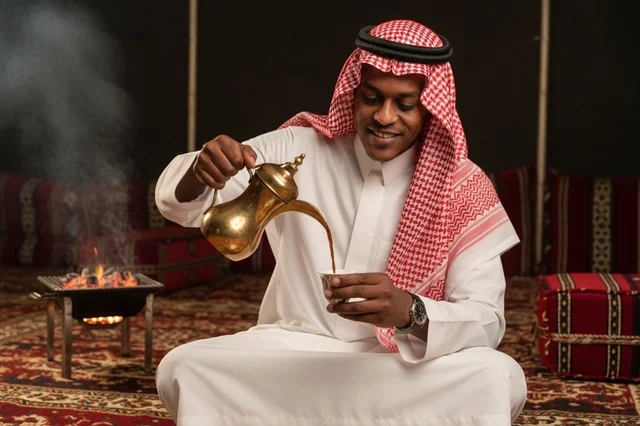 رجل سعودي بالزي التقليدي يصب القهوة العربية في خيمة