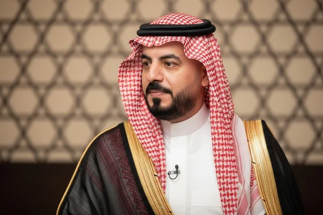 A Saudi man wearing a black bisht and traditional red shemagh.