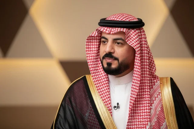 A Saudi man wearing a black bisht and traditional red shemagh.