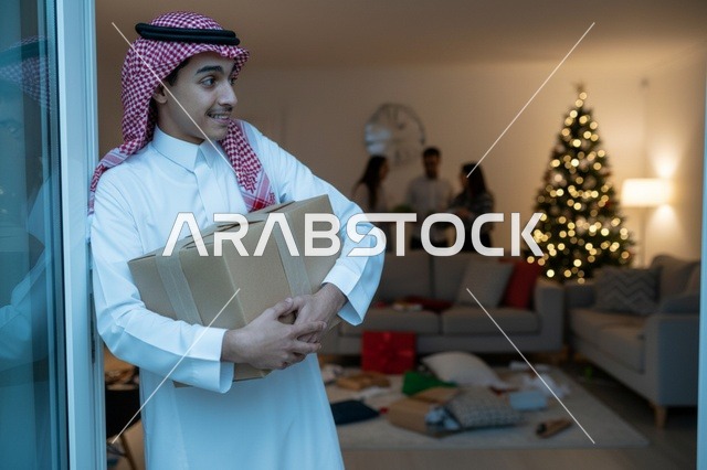 رجل سعودي يحمل صندوق هدايا بجوار شجرة الميلاد