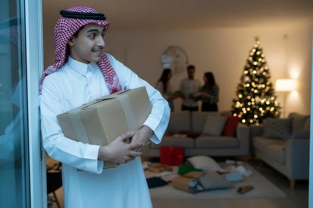 رجل سعودي يحمل صندوق هدايا بجوار شجرة الميلاد