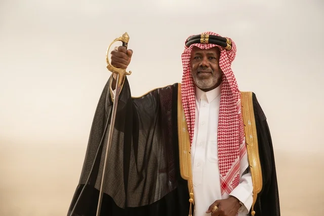 رجل سعودي بالبشت التقليدي يمسك سيفاً في الصحراء