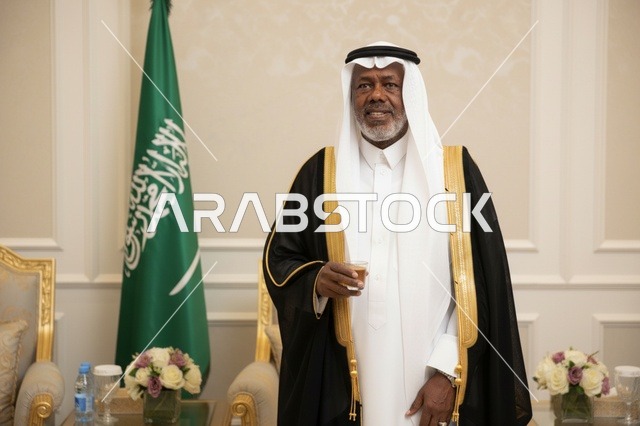 رجل سعودي بالبشت الرسمي بجانب العلم الوطني