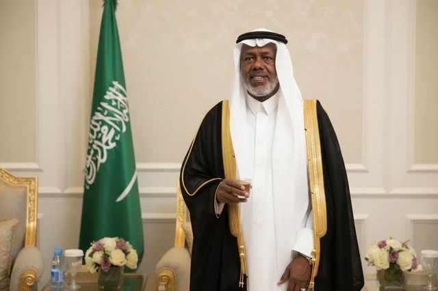 رجل سعودي بالبشت الرسمي بجانب العلم الوطني