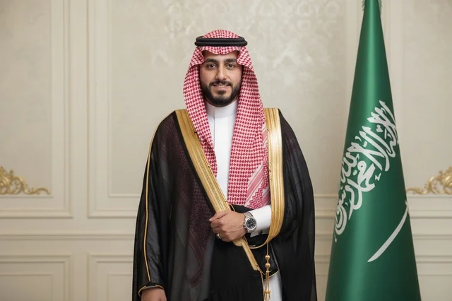 رجل سعودي بالزي الرسمي مع علم المملكة العربية السعودية