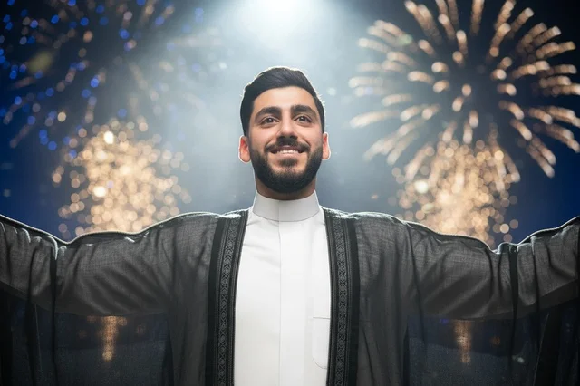 رجل سعودي بالبشت التقليدي مع ألعاب نارية ليلاً