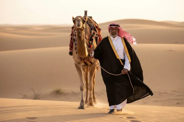 رجل سعودي مع جمل في الصحراء وقت الغروب